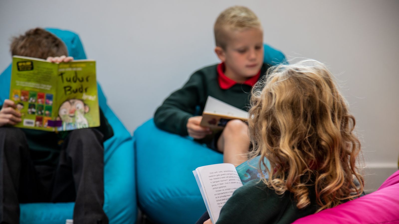 Three children sitting on bean bags, each engrossed in reading a book.