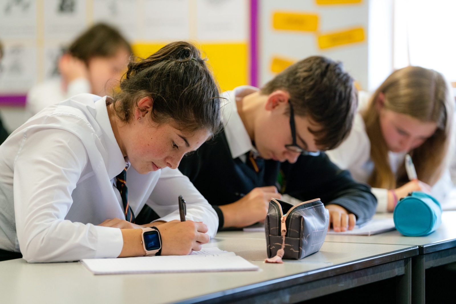 Three students in school uniforms diligently writing in their notebooks during a classroom activity