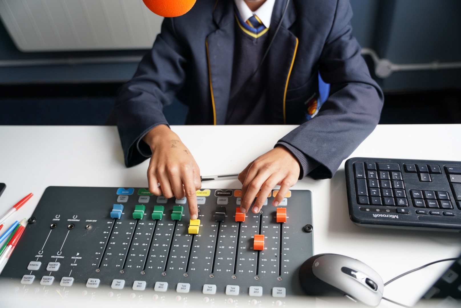 Close-up of a student’s hands adjusting the controls on a soundboard in a school radio studio.