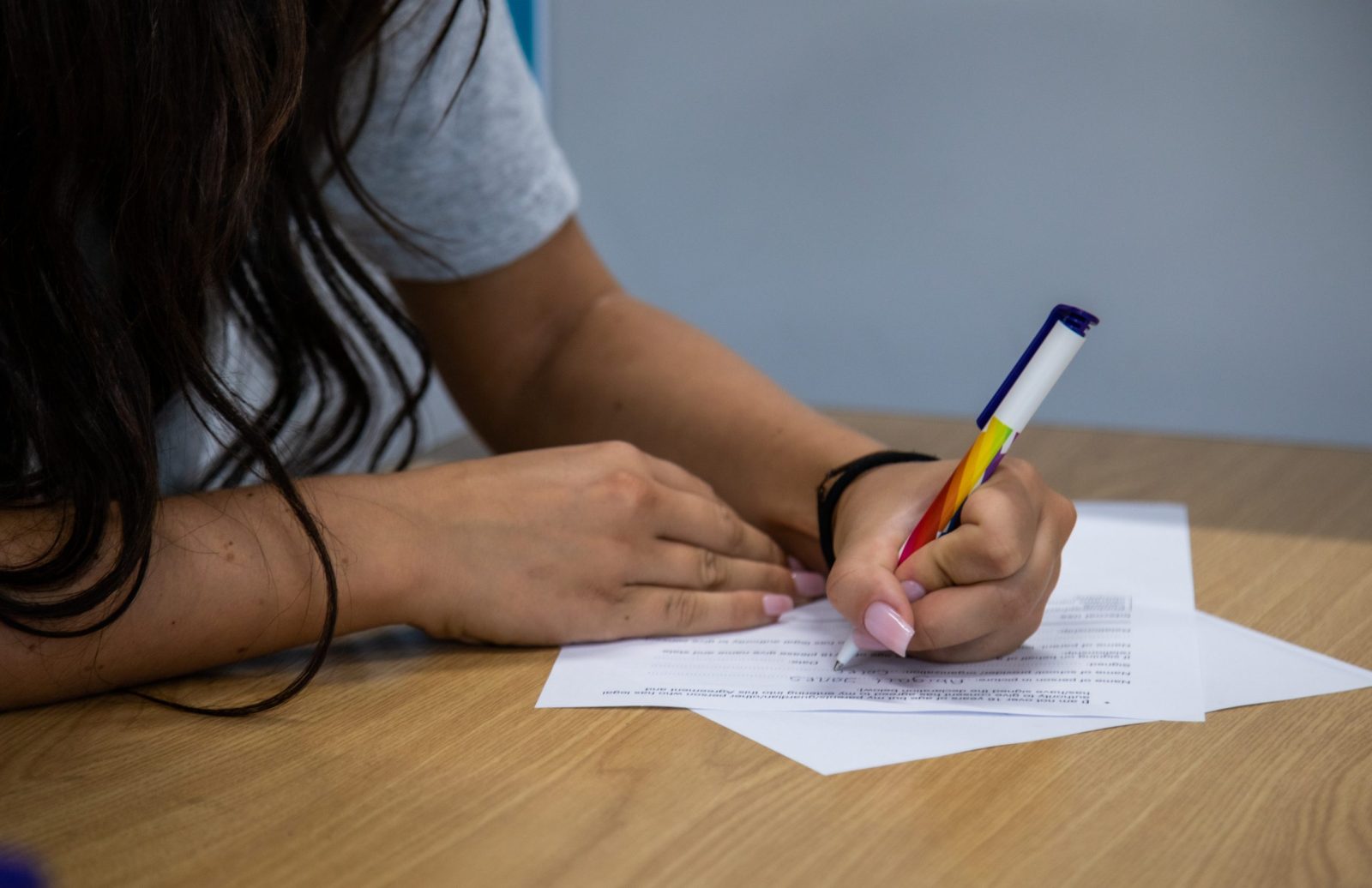 Close-up of a student's hands holding a pen while writing on a piece of paper on a wooden desk.