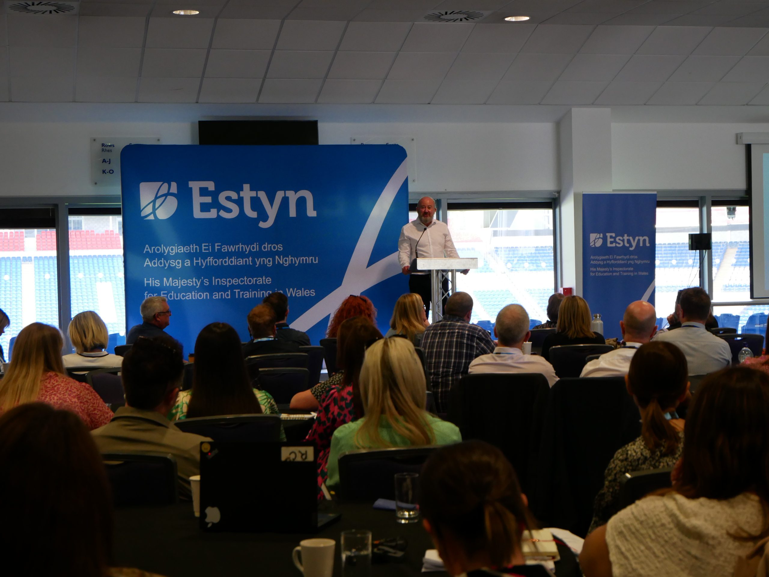 Owen Evans stands confidently at a podium, delivering a presentation to an engaged and attentive large audience.