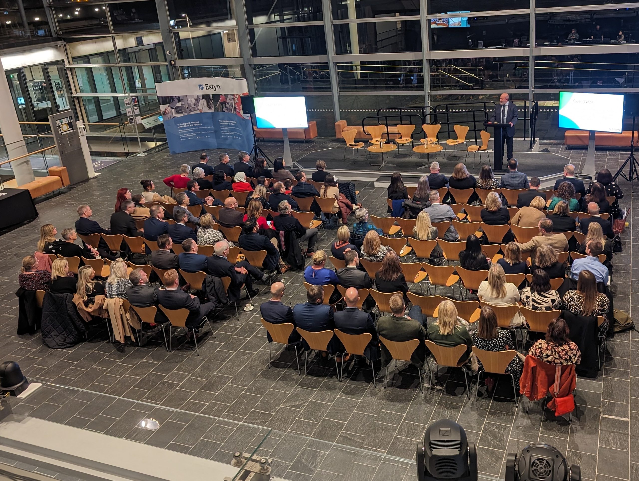 A large crowd seated in chairs within a spacious room during the Estyn annual report at the Senedd.