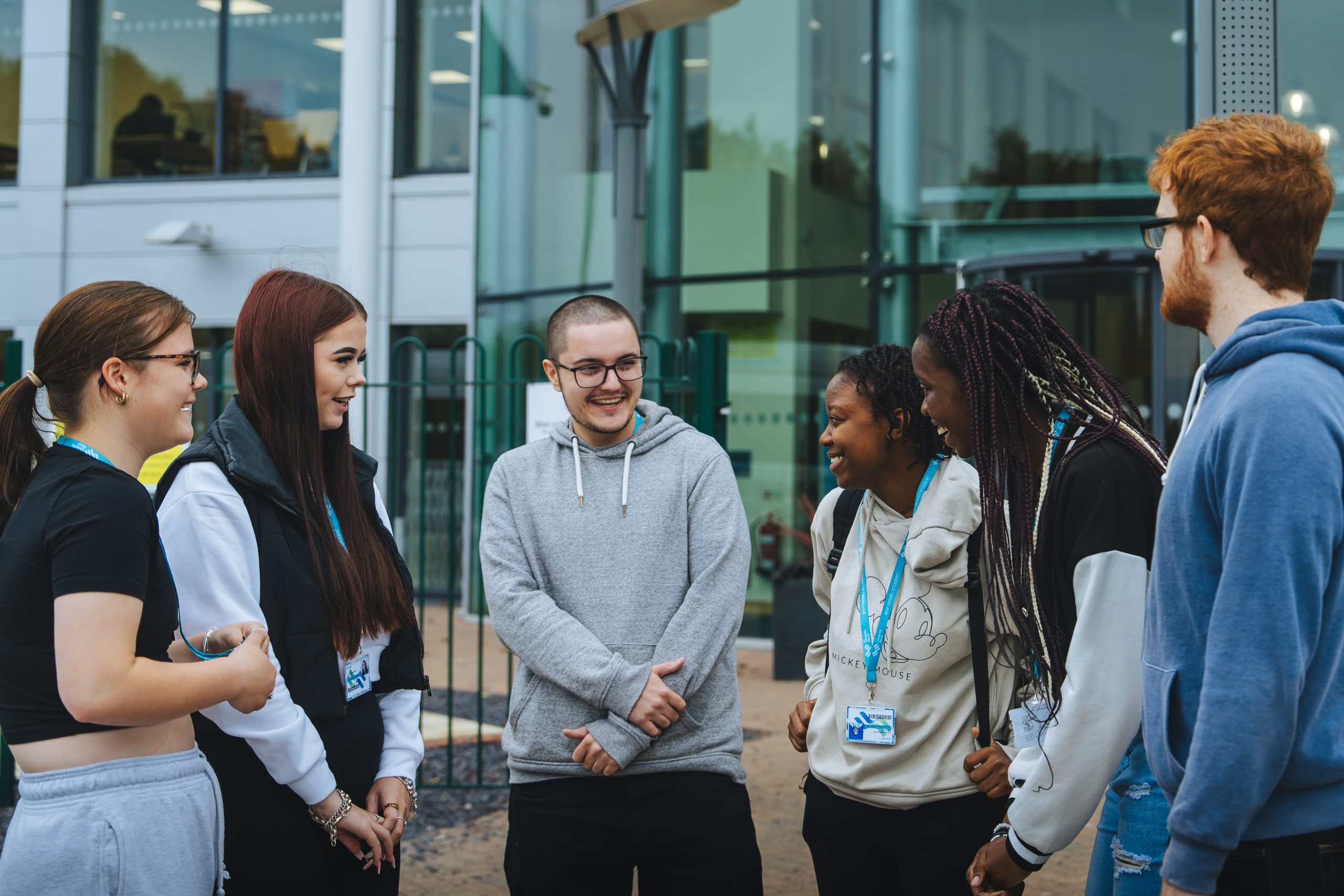 A group of students stand outside a modern building, smiling and engaged in conversation.