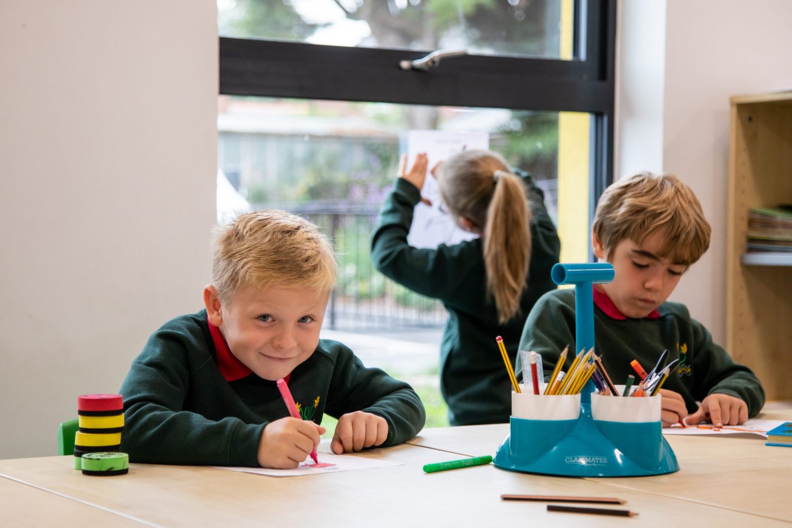 Young children drawing and coloring at a table in a classroom.