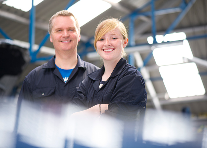 A man and woman wearing overalls in a hanger smiling at the camera.