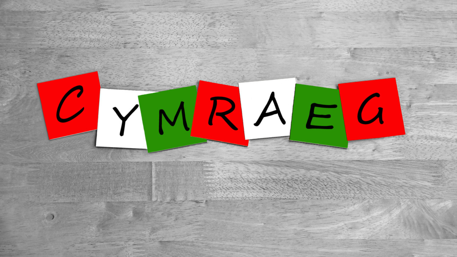 Colorful cards spelling out "CYMRAEG" on a wooden background.