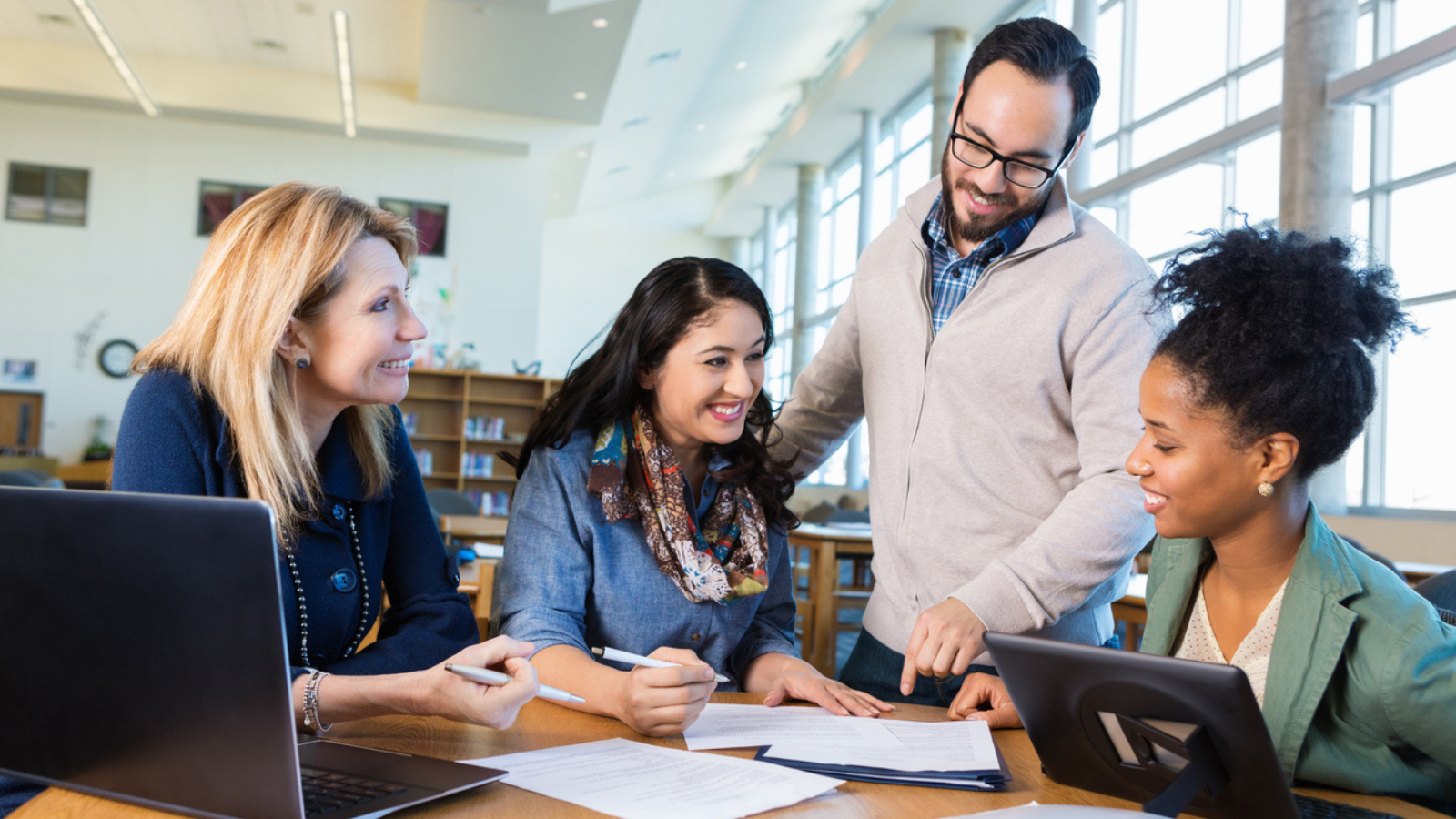 Four professionals collaborate at a table with a laptop in a well-lit office space.