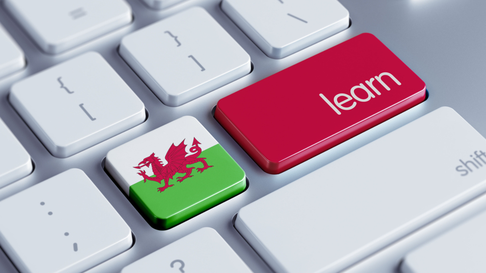 A computer keyboard with two custom keys: one green with the Welsh dragon emblem, and another red labeled 'learn'.