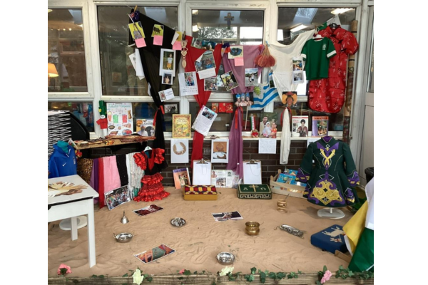 Display of cultural artifacts and memorabilia including traditional clothing, photographs, books, and decorative items, arranged in a window setup with a background of colorful notes and flags.