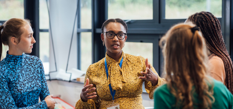 A person in a yellow outfit is engaged in a discussion with three colleagues in an office setting.