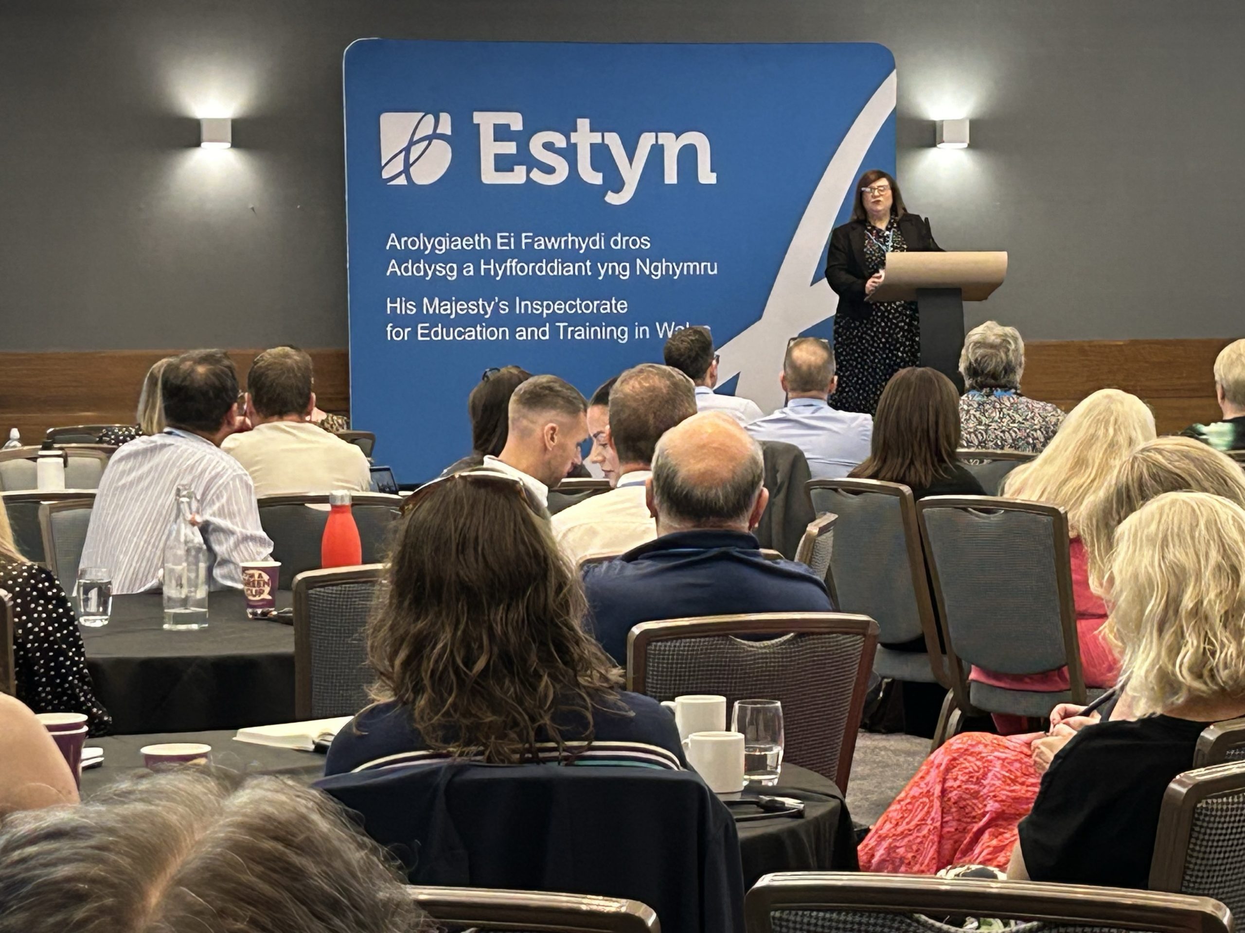 Person presenting at an Estyn conference in front of an audience.