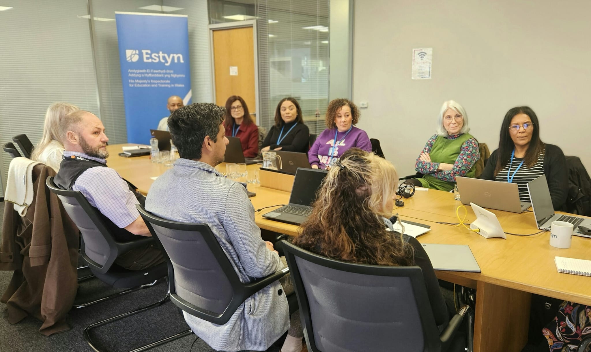 A group of professionals seated around a conference table during a meeting at an Estyn office.