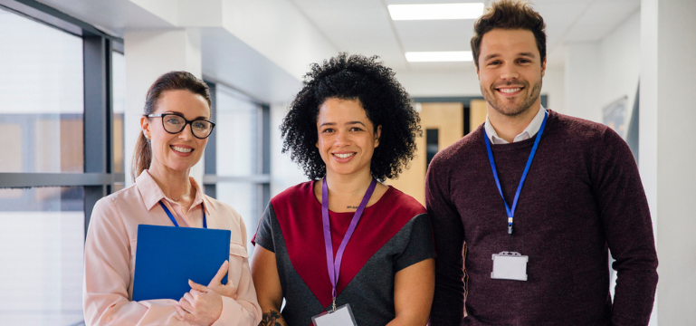 Three professionals with ID badges, smiling in an office hallway.
