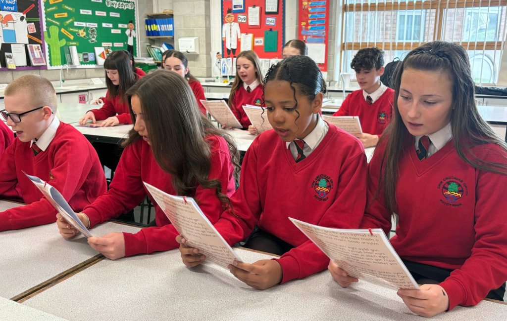 Students in red uniforms reading papers in a classroom.
