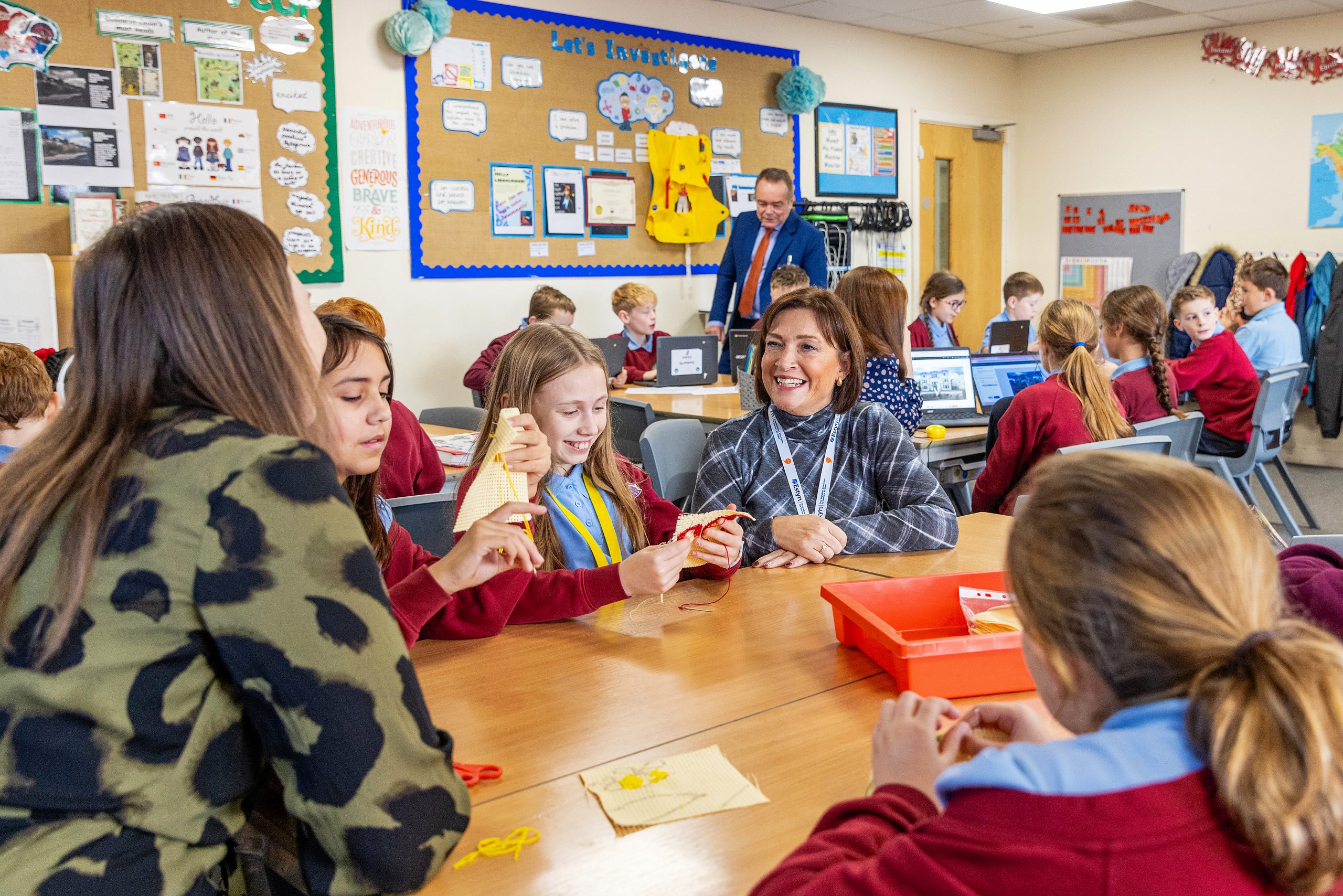 Students and a teacher engaged in an interactive activity in a classroom, with computers on desks and educational posters on the walls.