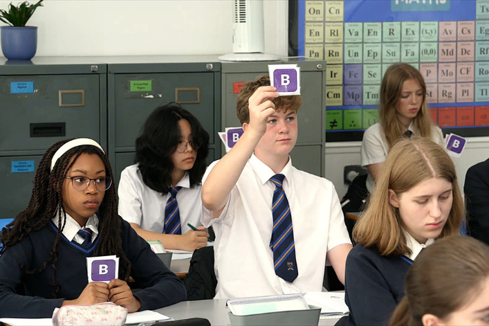 Students in a classroom holding cards with letters, participating in an educational activity.