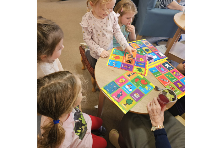 Four children and an elderly person playing a colorful board game at a table.