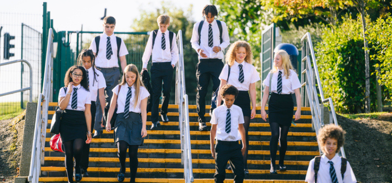 A group of school students in uniform walking down outdoor steps, with railings on both sides and greenery around them.