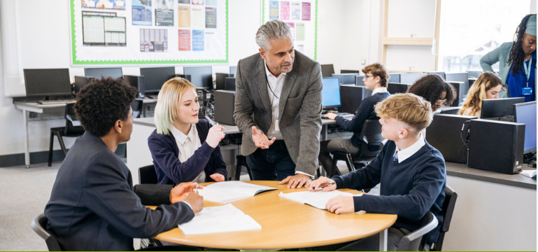 Teacher supporting students working together in a computer classroom.